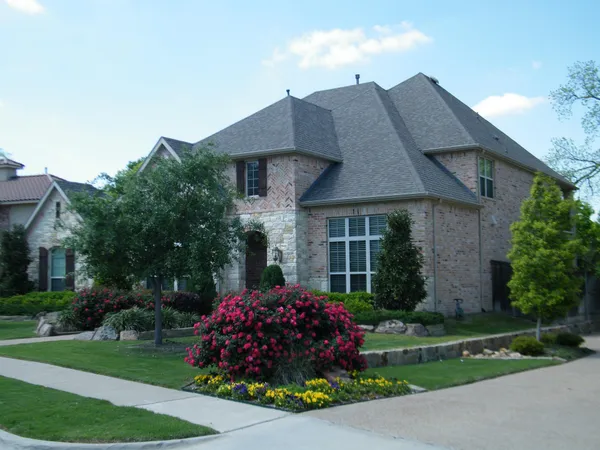 Exterior of a brick house with a lot of decorative foliage and bushes